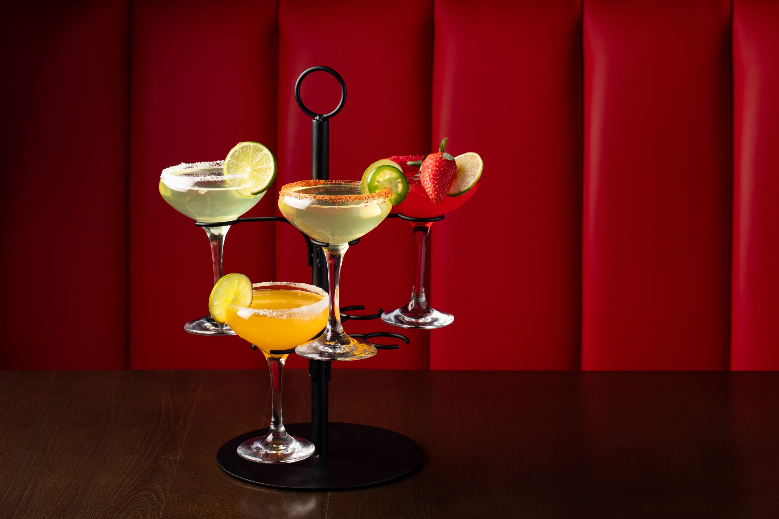 Assorted cocktails with fruit garnishes against red background in Waukegan, IL.