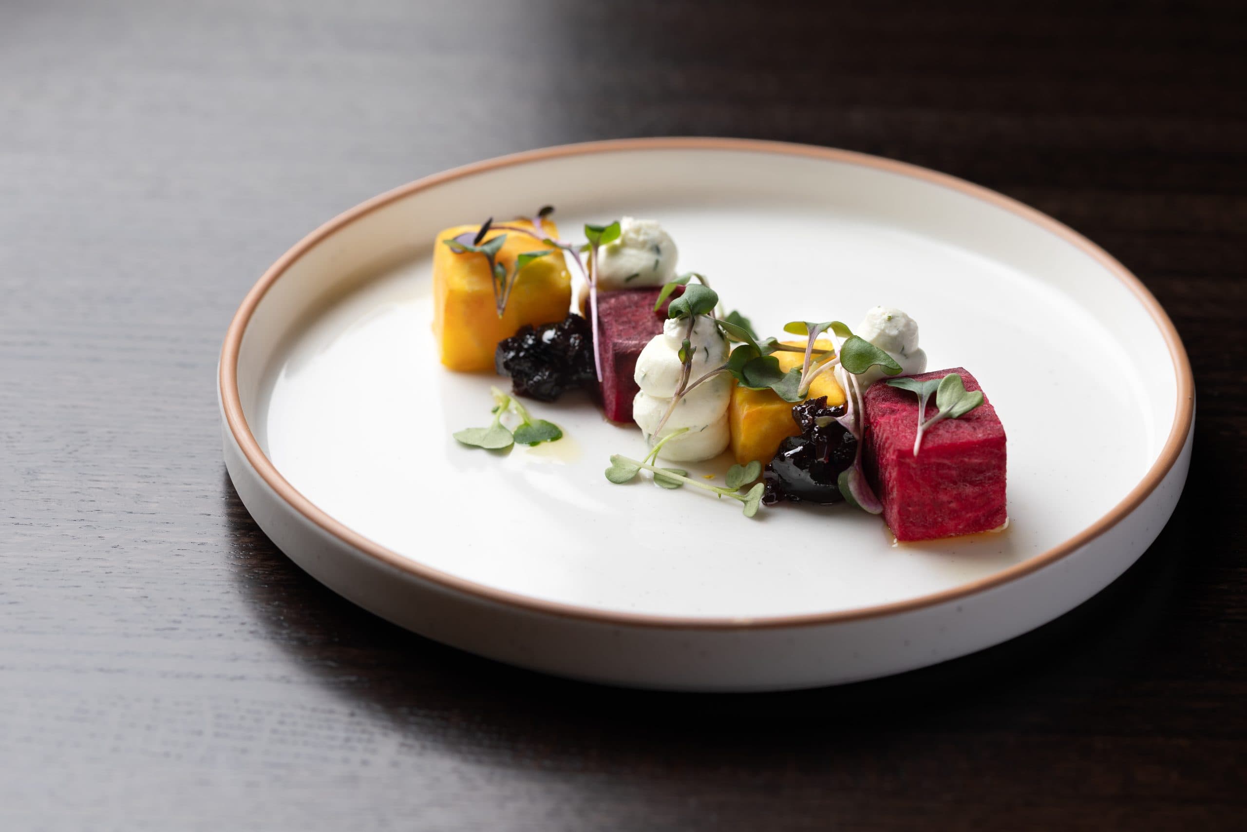 Colorful seafood dish with watermelon, mango, and microgreens on a white plate.